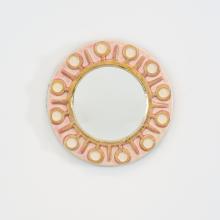 Miroir mural rond en céramique émaillée rose pâle et or de Mithé Espelt, modèle « Soleil ». Décor graphique stylisé aux motifs circulaires évoquant le rayonnement solaire, réalisé à la main dans les années 1950.